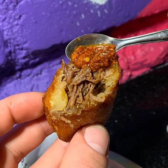 Bolinho de aipim partido ao meio na mão, mostrando o recheio de carne de panela.