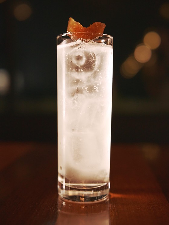 Caju Spritz servido num copo alto, com espuma densa no topo, sobre a mesa de madeira do salão.