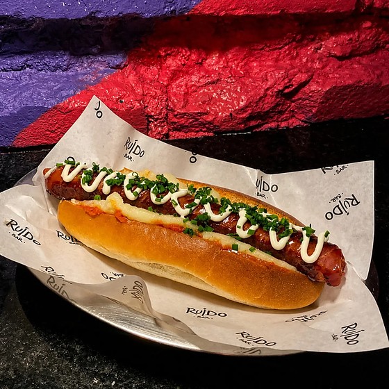 Cachorro-quente com linguiça, purê, maionese e ciboulette, servido no papel timbrado do Ruído.