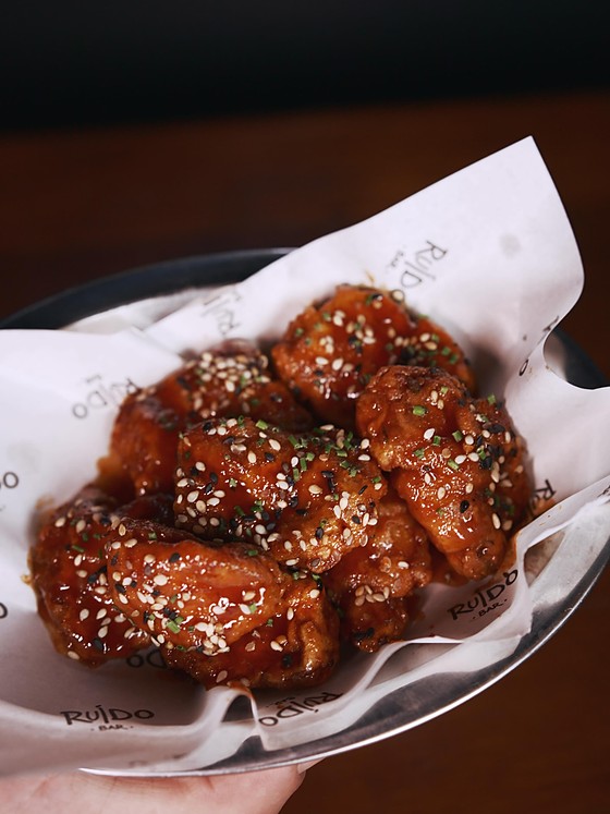 Franguinho gochujang: cubos de sobrecoxa empanados e lambuzados em molho escuro, com gergelim, servidos numa travessa branca.